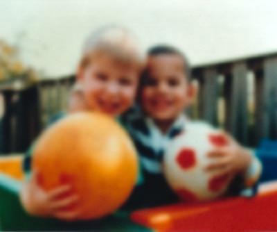 A blurry photo shows two boys with rubber balls. The photo shows how cloudy lenses in the eye, called cataracts, affect vision.