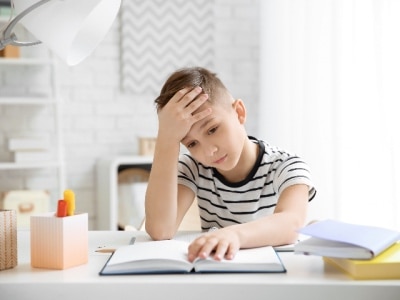 Young boy having trouble concentrating while doing homework at a desk.
