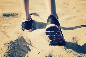 Photo of someone's feet wearing shoes and walking on the sand.