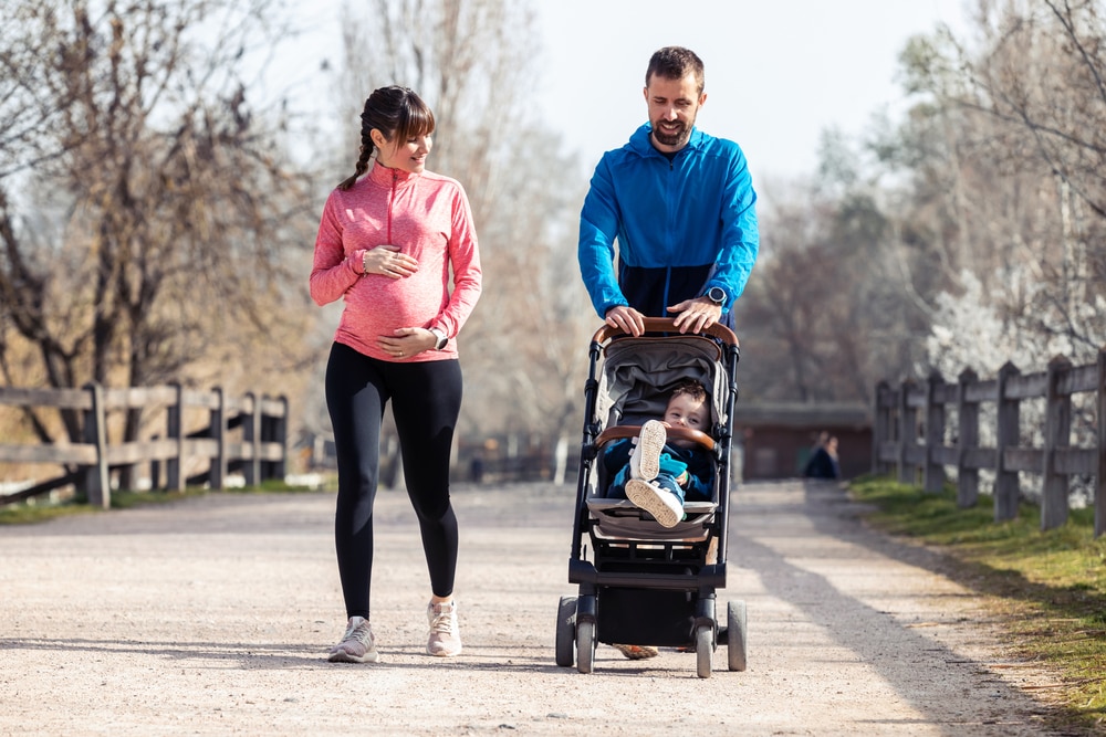 A man pushing a stroller with a baby outdoors and a pregnant woman walking next to them.