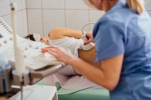 Una profesional de atención médica sostiene un transductor de ultrasonidos sobre la zona del riñón en la espalda de una paciente.