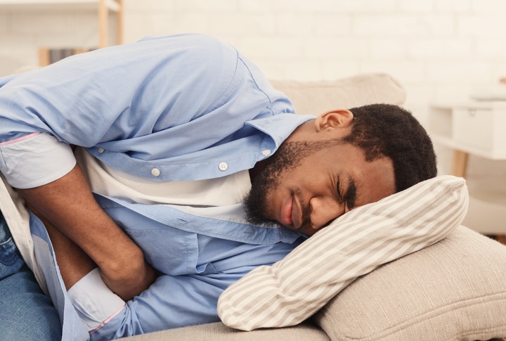 A man grimacing in pain while he lies on a sofa.