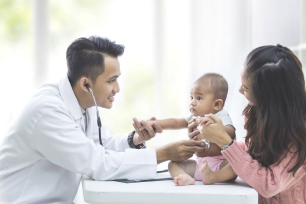 Médico usando un estetoscopio para escuchar el abdomen de un bebé.