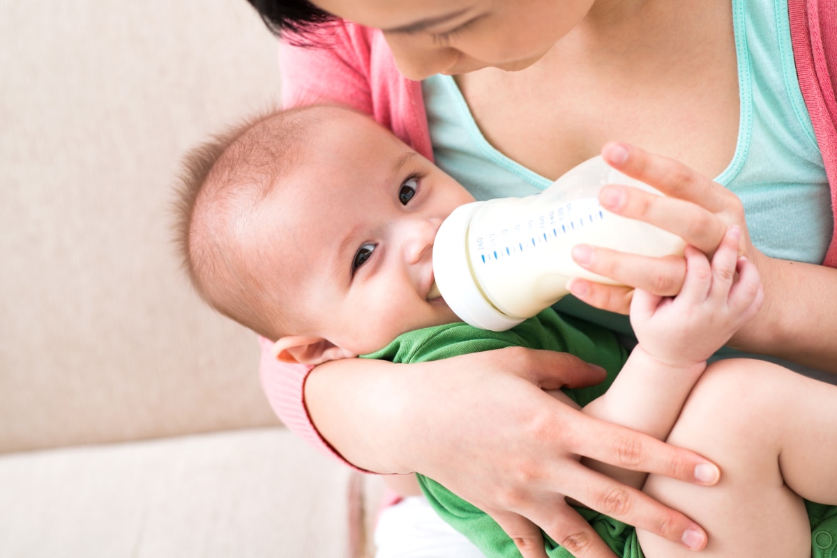 A woman feeds an infant a bottle of breast milk or formula.