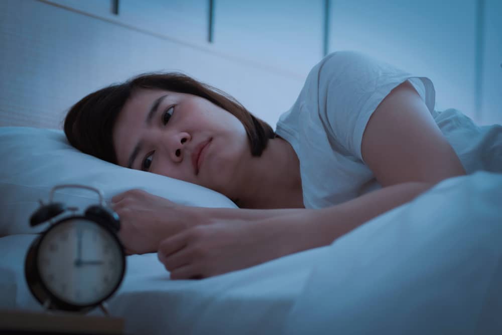 A woman lies awake in bed, facing a clock that reads 3 o'clock.