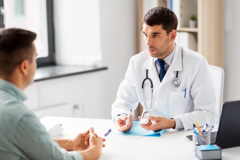 A health care professional talks about diabetes equipment with a man seated across a desk.