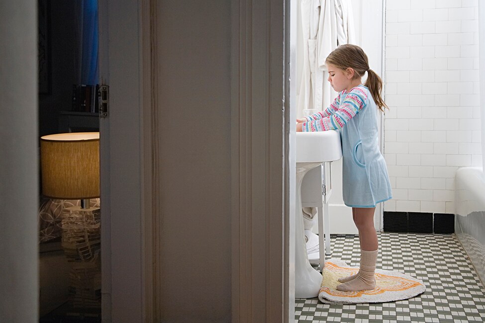 منظر من رواق يظهر فتاة تغسل يديها في الحمام بجوار غرفة نومها.