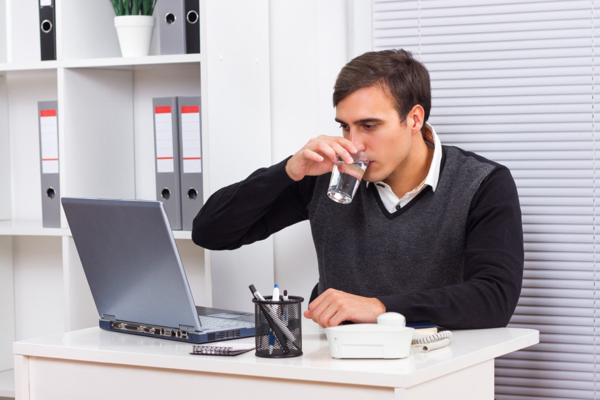 Man sitting at a desk, drinking a glass of water.