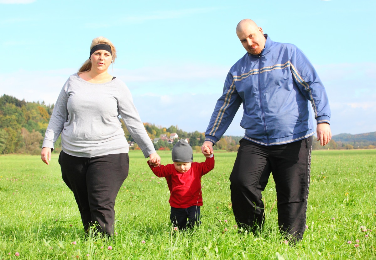Un hombre y una mujer con sobrepeso caminan en un campo abierto con un niño pequeño.