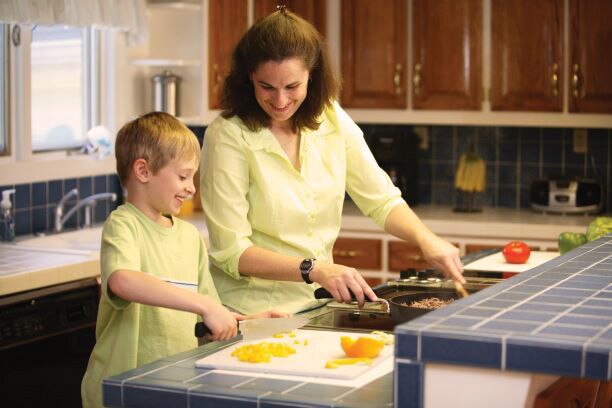 Mother and school-age son prepare a meal in their kitchen.