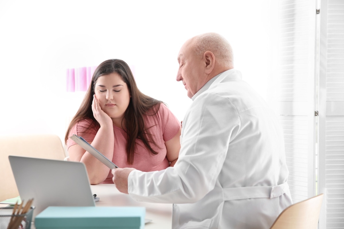 Un profesional de atención de salud habla con una mujer que tiene obesidad, en su consultorio.