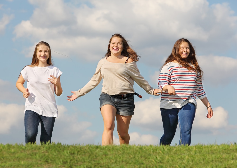 Tres jovencitas adolescentes caminan juntas al aire libre.