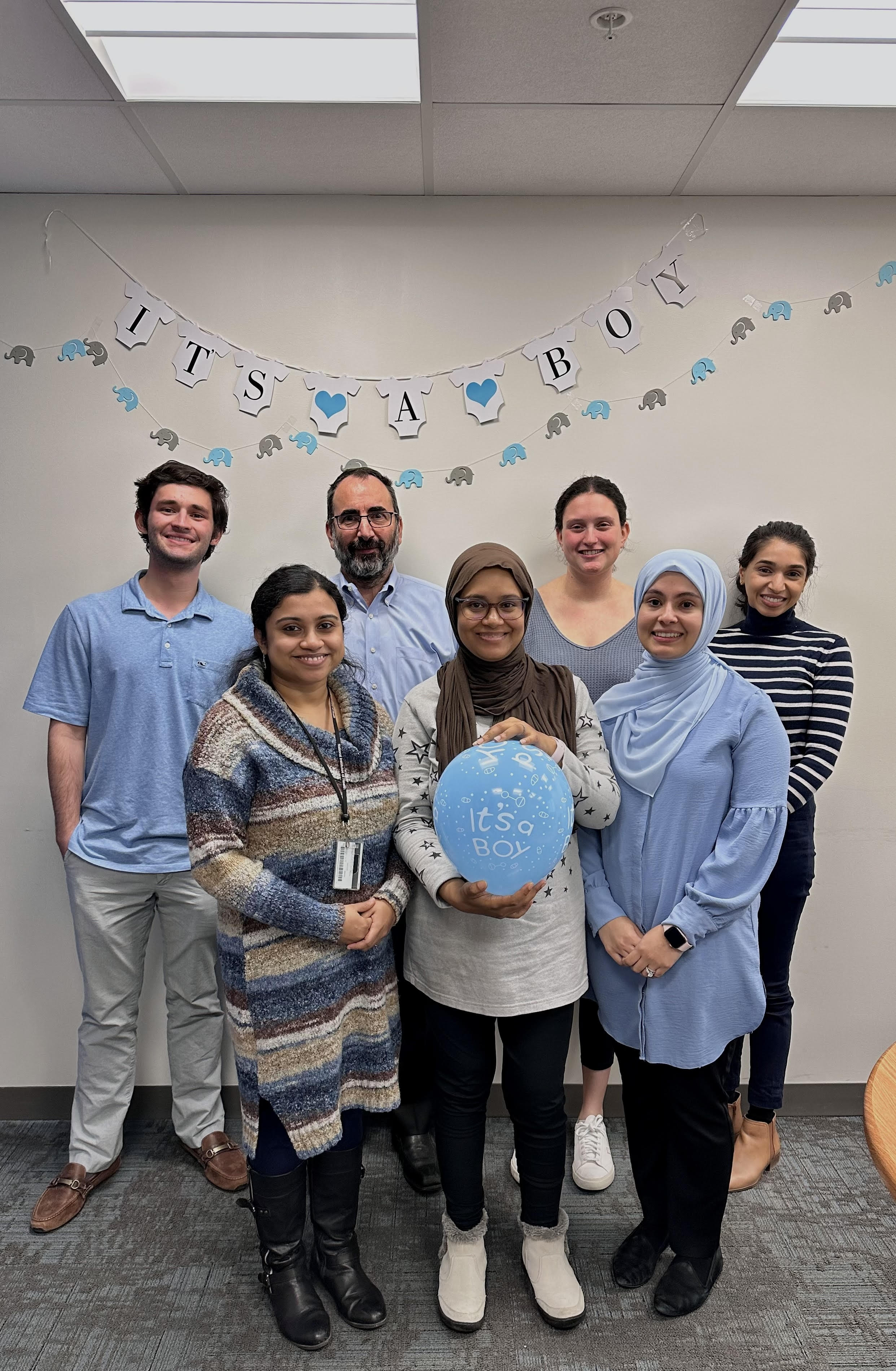 Lab Members in front of a banner that says "It's a Boy".  One member is holding a blue balloon.