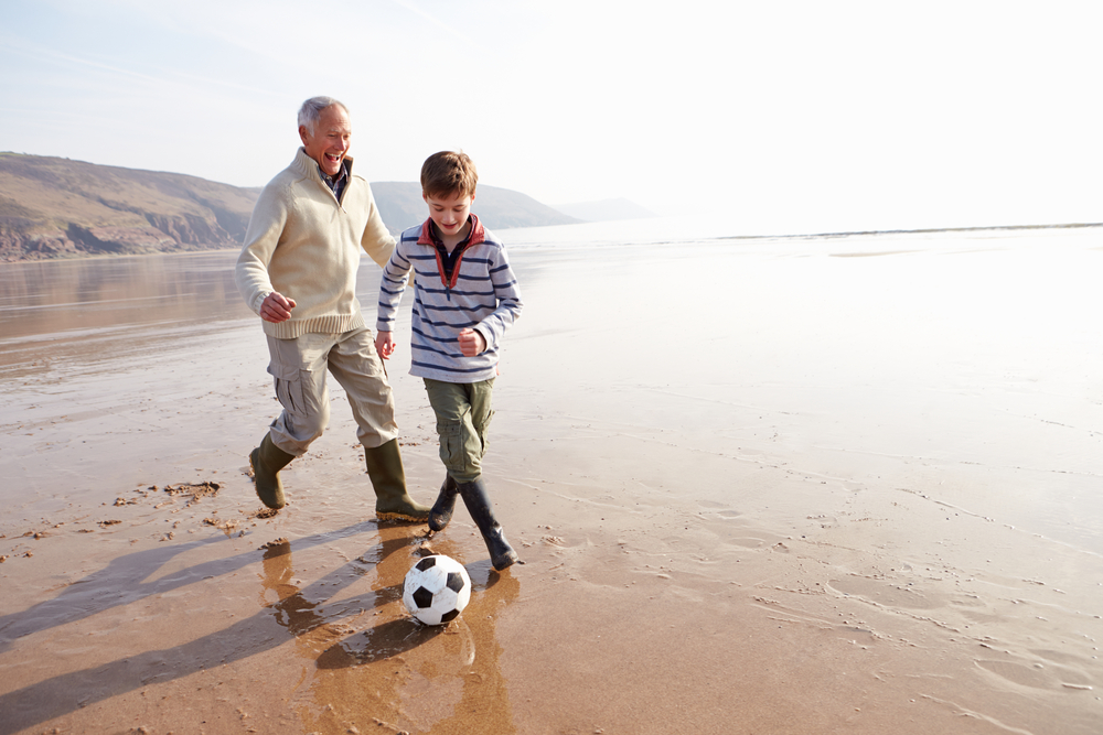 Un abuelo juega fútbol con su nieto en la playa.